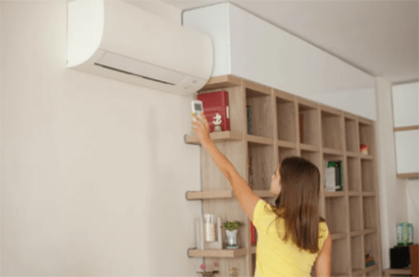 a girl turns on wall-mounted air conditioner at home with remote control